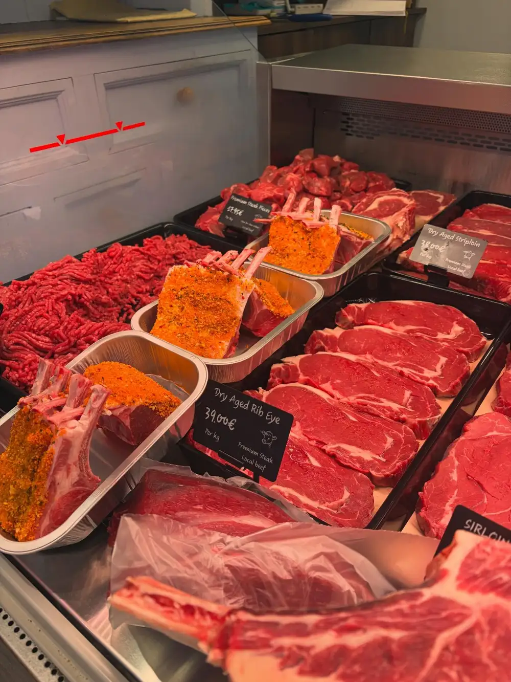 Dry-aged rib eye steaks and racks of lamb in the counter with a handwritten Dry Aged Rib Eye ticket