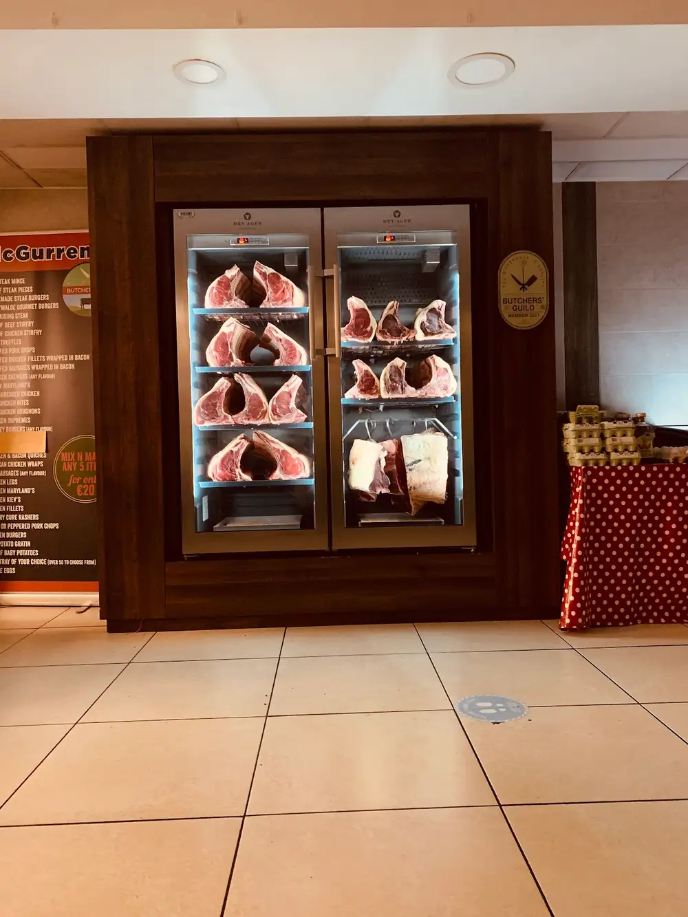 The in-store dry-aging cabinet hung with beef, beside the Irish Butchers' Guild plaque