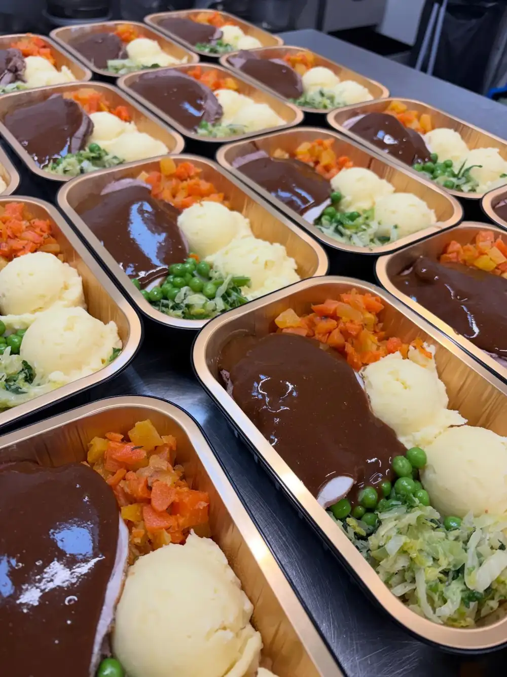 Rows of cooked dinner trays - roast meat with gravy, mash, peas and carrots