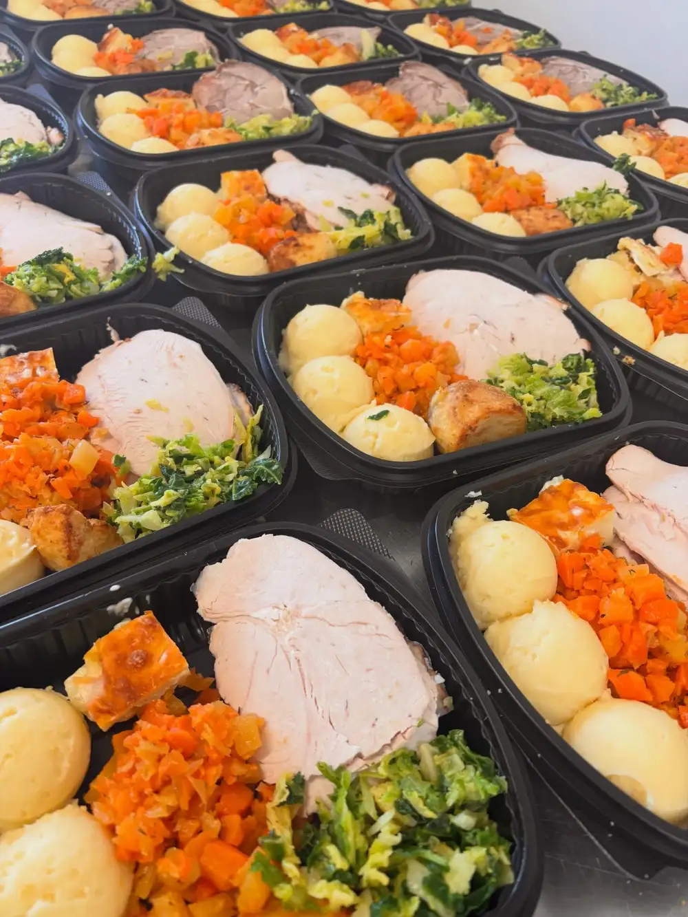 Trays of sliced turkey dinners with potatoes and vegetables lined up in the kitchen